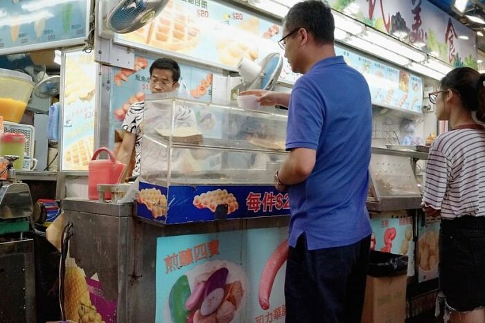Street coincidences caught on camera showing customers ordering snacks at a busy outdoor food stall in an urban setting.