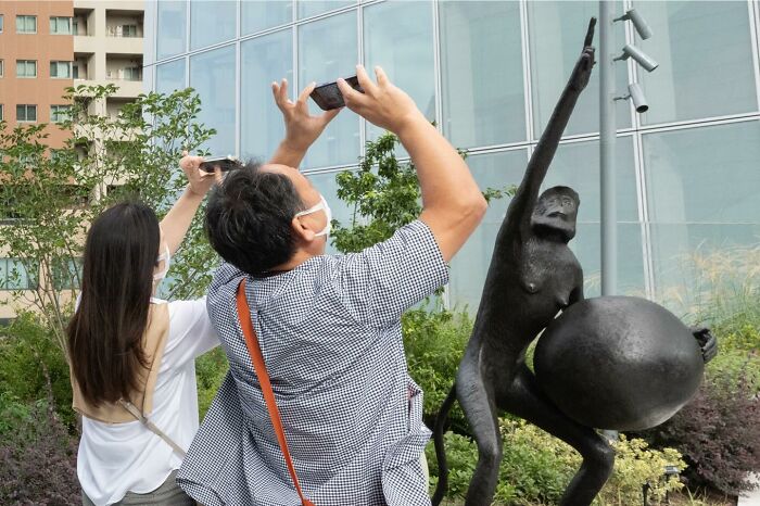 Two people wearing masks taking photos of a street statue, showcasing unbelievable street coincidences caught on camera.
