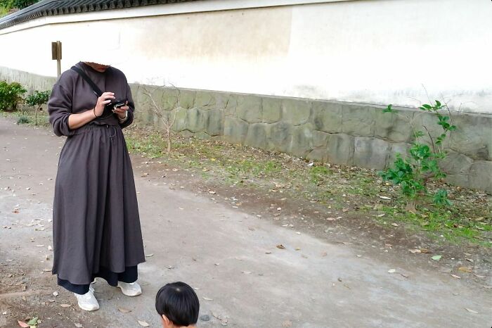 Woman wearing dark dress and white shoes using a camera on a street, capturing unbelievable street coincidences.