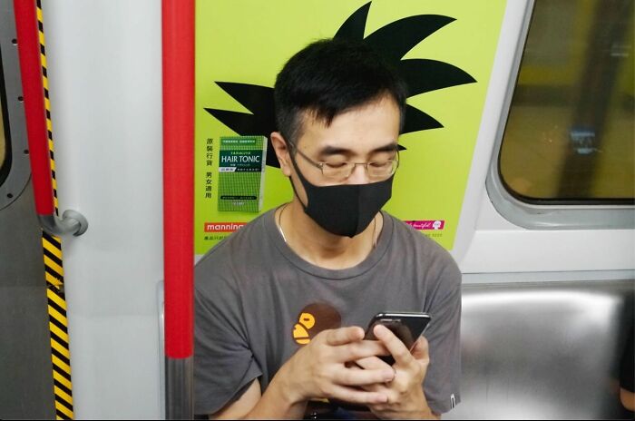 Man wearing glasses and black mask on train with hair silhouette creating a street coincidence effect.