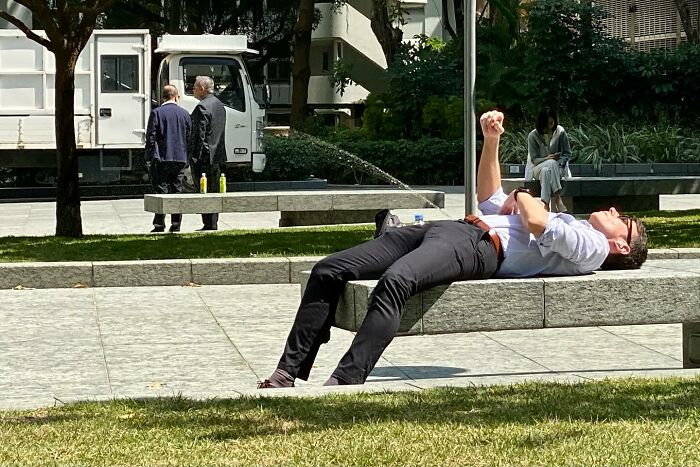 Man lying on a bench in a park with water appearing to spray from his hand in an unbelievable street coincidence moment
