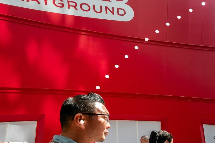 Man wearing glasses and earbuds walking past a bright red wall, illustrating unbelievable street coincidences caught on camera.
