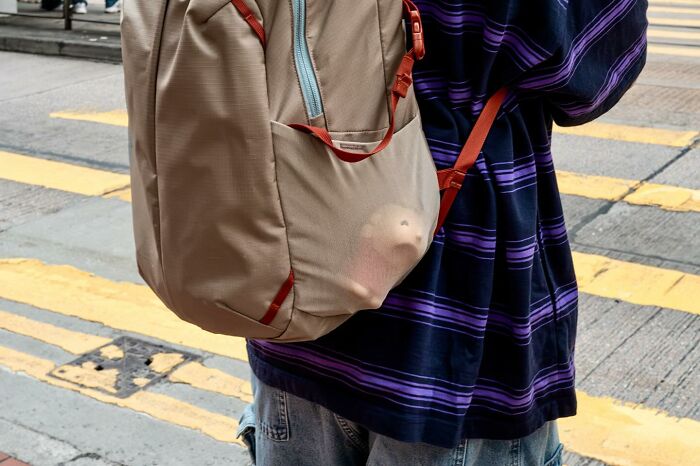 Person wearing striped shirt and backpack with a small smiling face visible through the fabric on a street corner, street coincidences.