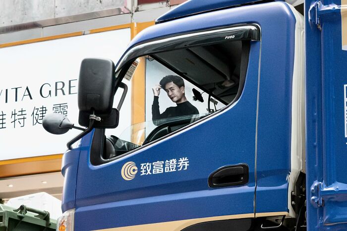 Man on advertisement aligns perfectly with truck window, a street coincidence captured by Edas Wong.