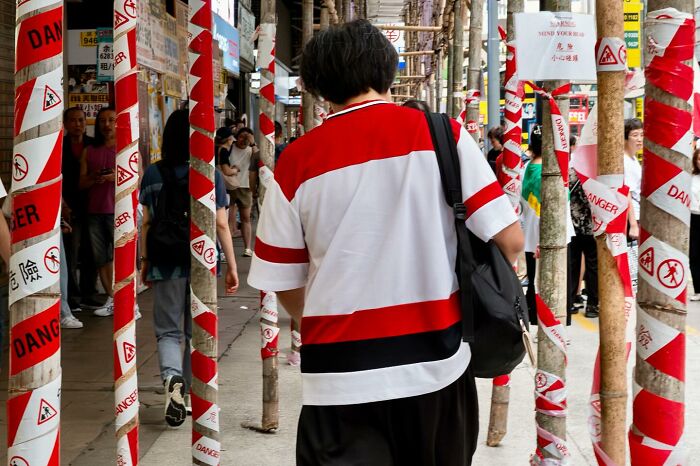 Person walking through a street with poles wrapped in red and white danger tape, showing street coincidences caught on camera.