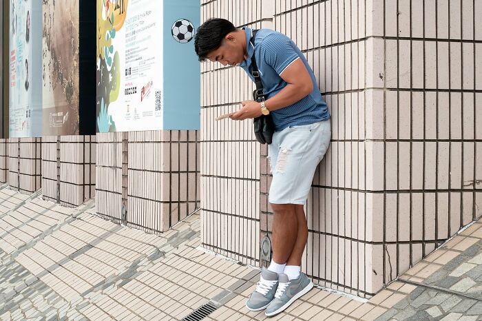 Man pretending to kick a cartoon soccer ball on a tiled street wall in an unbelievable street coincidence scene.