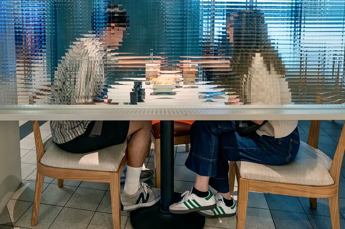 Two people sitting opposite each other at a table, with a distorted glass effect resembling street coincidences captured on camera.