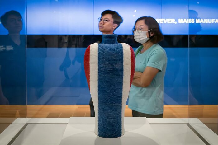 Ceramic vase with red, white, and blue stripes displayed in a museum with visitors observing behind glass.