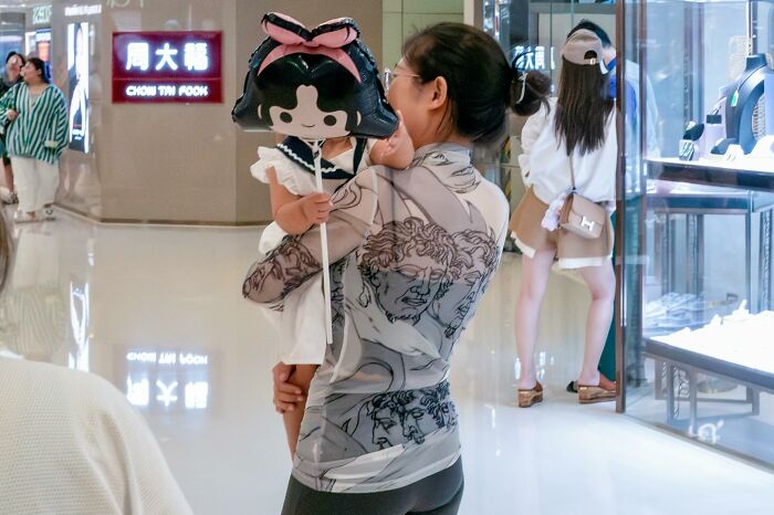 Woman holding child with cartoon balloon in shopping mall showing street coincidences caught on camera.