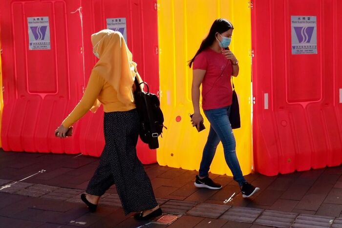 Two women walking past bright yellow and red barriers, illustrating street coincidences caught on camera.