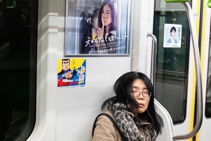 Woman appears to shush with finger near lips on poster above sleeping woman on train in street coincidences photo.