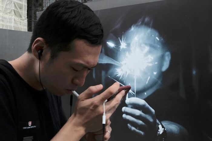 Man lighting cigarette in front of a mural showing a sparkler, a street coincidence caught on camera.
