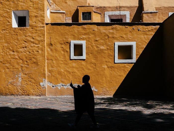 Silhouette of a person walking past textured yellow walls in a street photography shot capturing life realistically.