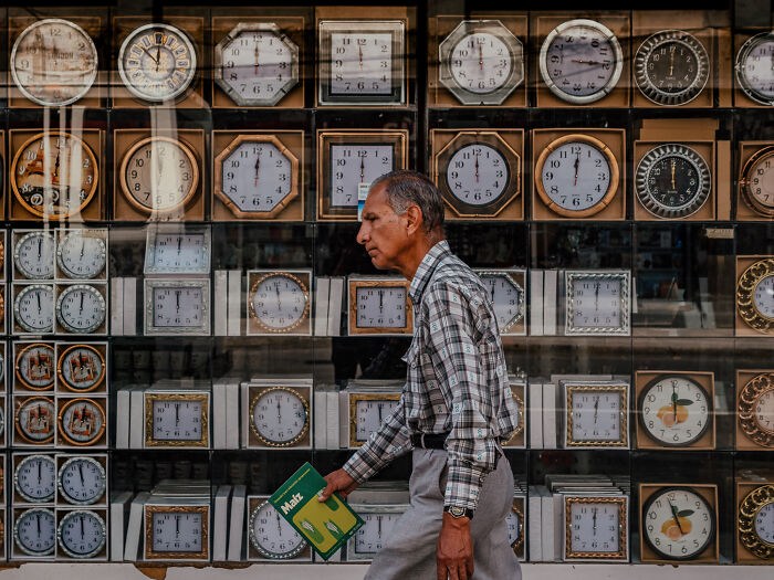 Man walking past a store window filled with various clocks, showcasing street photography shots capturing life realistically.