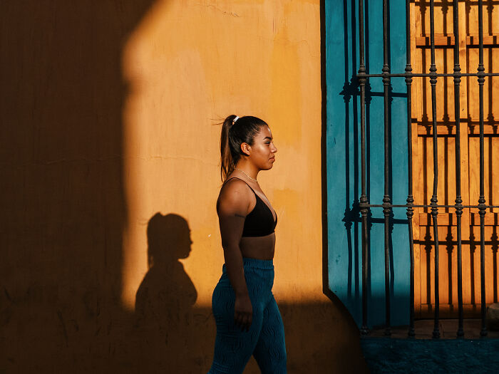 Woman walking past orange and blue wall with shadow in a vibrant street photography shot capturing life as it really is.