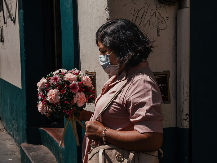 Woman wearing mask holding a bouquet of flowers in warm light, street photography shot capturing life as it really is