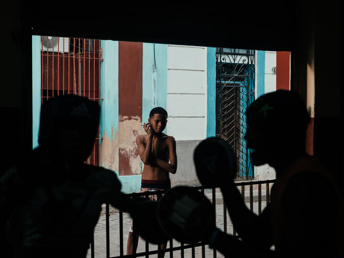 Street photography shot of a young boy observing two men boxing in a dimly lit urban setting.