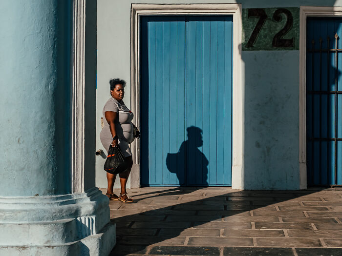 Woman standing near blue door with strong shadows in street photography capturing life as it really is.