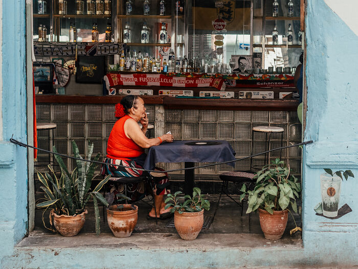 Woman in red top sitting at a table in a street photography shot capturing life as it really is in an urban setting