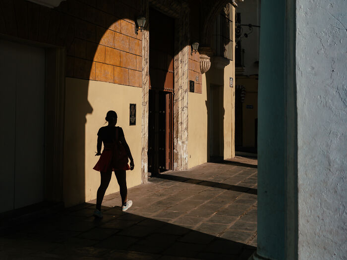Silhouette of a person walking through sunlit urban street, capturing authentic moments in street photography shots.