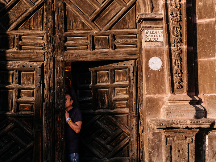 Man peeking through large wooden door in street photography shot capturing life as it really is in urban setting