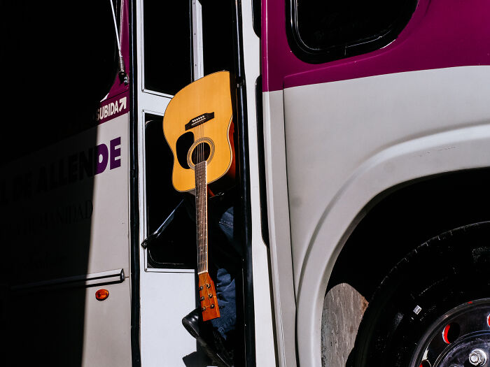 Guitar hanging as person boards bus, capturing candid street photography moments in urban life scenes.