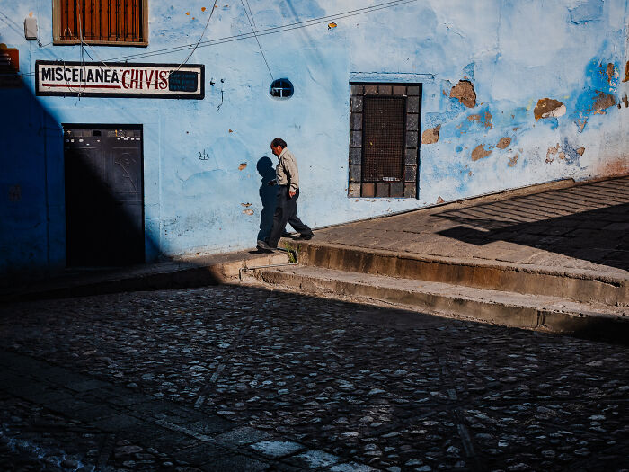 Man walking on steps beside a weathered blue wall in a street photography shot capturing life realistically.