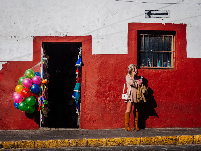 Street photography shot of a woman in boots standing by a colorful doorway and textured red and white wall.