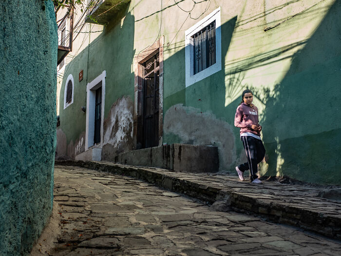 Young woman walking down a narrow cobblestone street in vibrant urban setting captured in street photography.