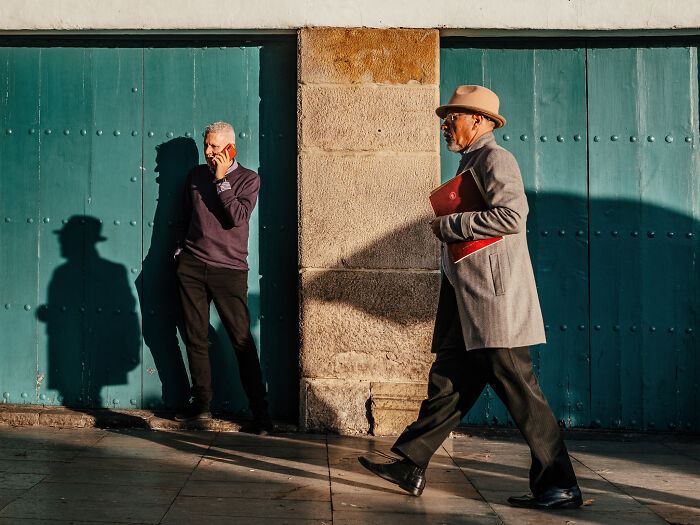Two men captured in street photography, one walking with a hat and coat, the other leaning and talking on a phone.