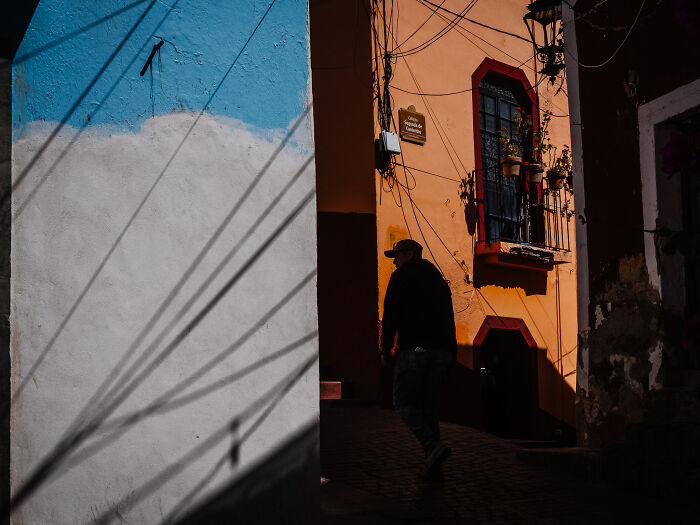 Man walking in a narrow street with colorful walls, showcasing authentic street photography shots capturing life.