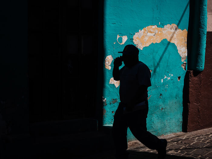 Silhouette of a man walking past a weathered turquoise wall in vibrant street photography capturing life as it really is.