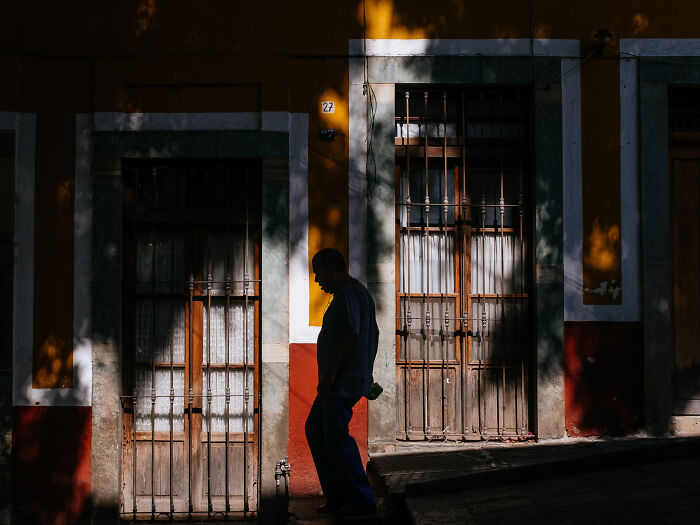 Silhouetted man walking past colorful buildings in warm light, a striking street photography shot capturing real life moments.