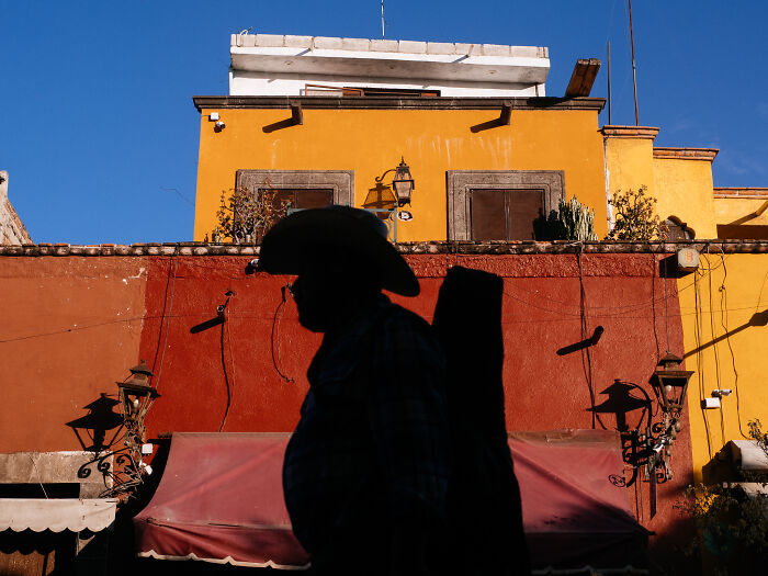 Silhouette of a man walking past vibrant colored buildings in a street photography shot capturing life naturally.