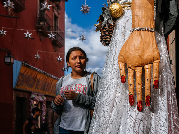 Woman walking on a street adorned with star decorations next to a large sculpture, captured in street photography.