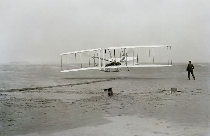 Early 20th century historic flight with the Wright brothers' first powered airplane taking off on a barren field.