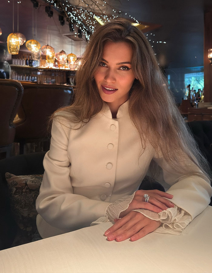 Former Miss Universe contestant, 30, sitting at a table in a cozy restaurant with soft lighting and festive decor.