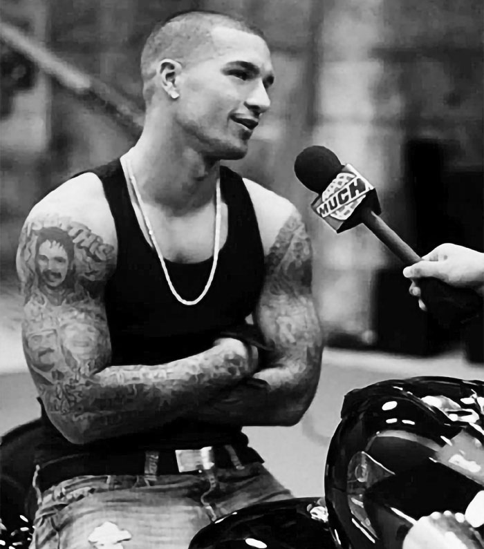 Tattooed man in black tank top being interviewed with a microphone, related to celebrities and disappearances unsolved.