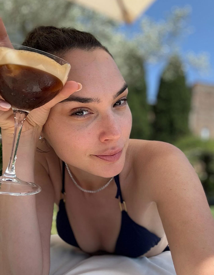 Gal Gadot relaxing outdoors in a black bikini, holding a drink, amid career challenges as an actress. Gal Gadot relaxing outdoors in a black bikini, holding a drink, amid career challenges as an actress.