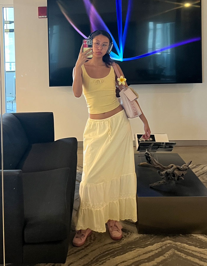 Gen Z worker takes mirror selfie in yellow outfit, sparking discussion about inappropriate office dress code and defense from netizens.