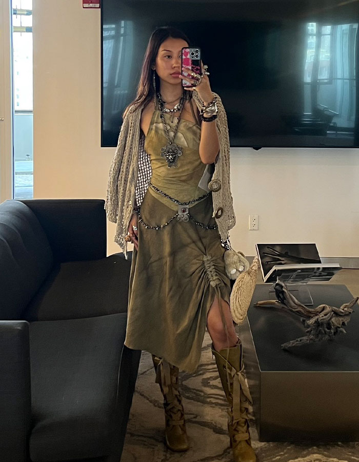 Gen Z worker taking a mirror selfie wearing a stylish dress and accessories, sparking debate on office dress code.