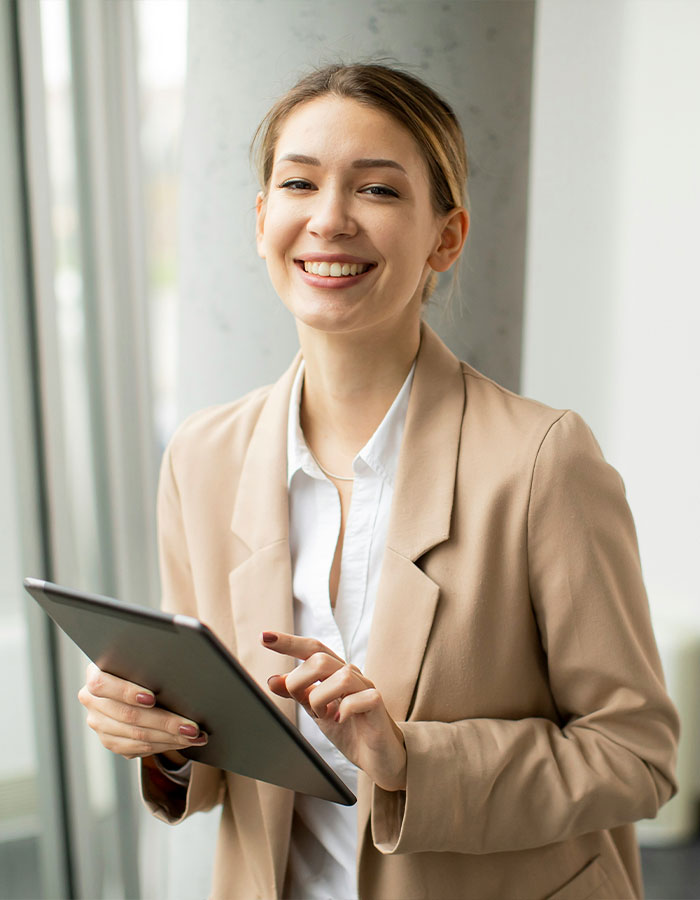 Young Gen Z worker in beige blazer smiling while using a tablet, representing office dress code debate and netizen defense.