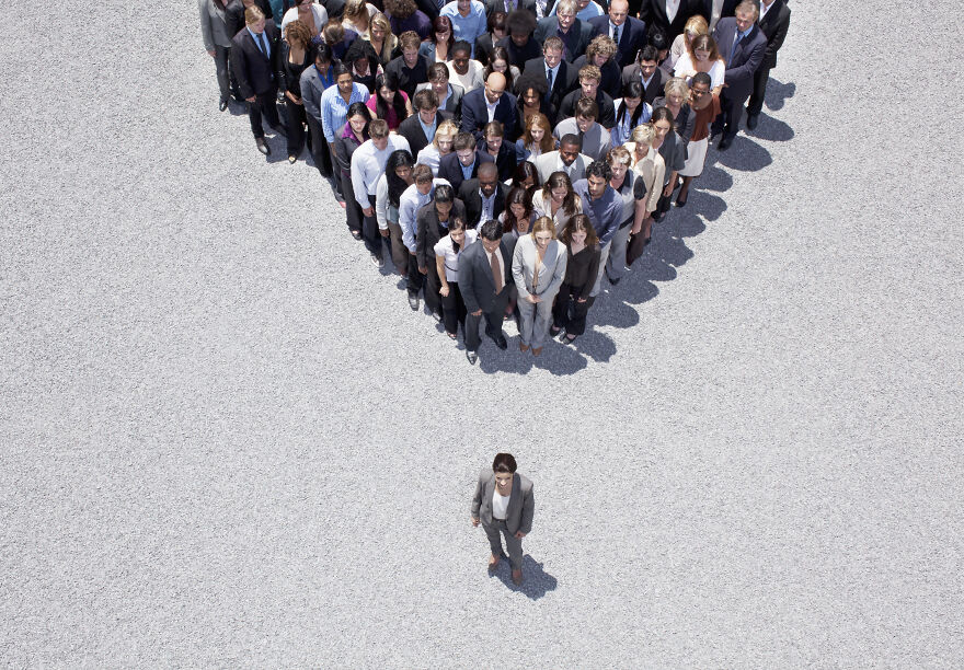 A lone businesswoman standing apart from a large group shaped to form an arrow, symbolizing Maslow&rsquo;s hierarchy concept.