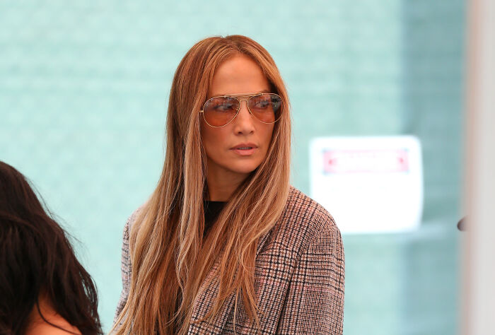 Jennifer Lopez wearing sunglasses and a plaid jacket, in a public setting related to Chanel brand controversy.