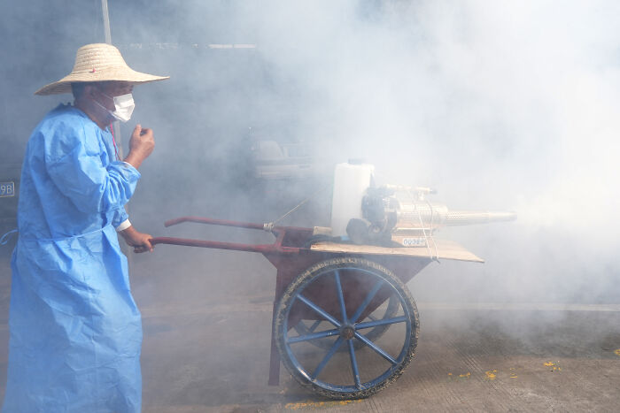 Person in protective clothing and mask fumigating outdoors to control chikungunya outbreak risks in China.