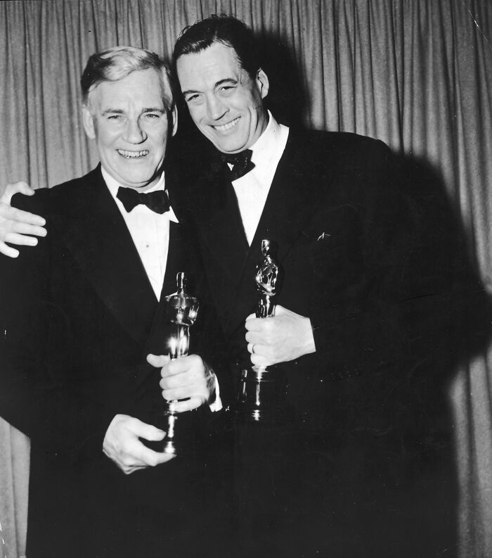 Two men in tuxedos holding Oscars, representing legendary entertainment families passing the spotlight through generations.