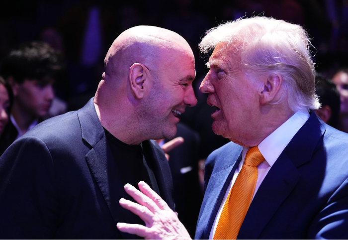 Dana White in a dark suit smiling and speaking closely with a man in a blue suit and orange tie at a UFC event.