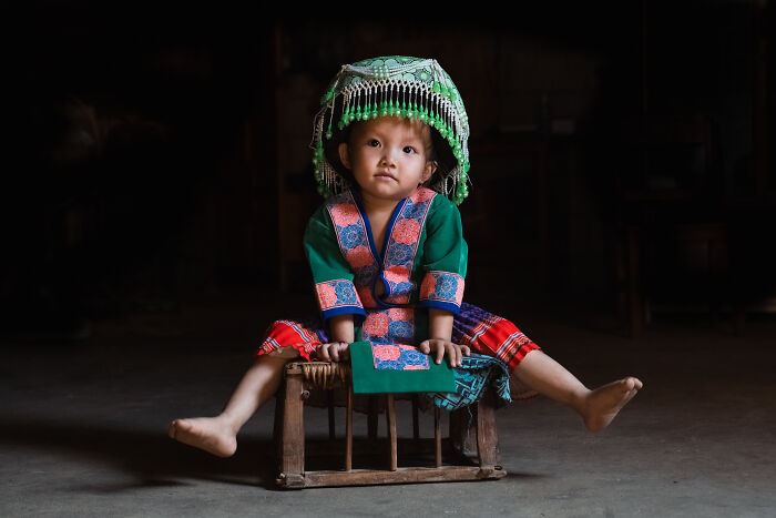 Young child in traditional colorful cultural attire sitting on a wooden stool, capturing the beauty of cultures.