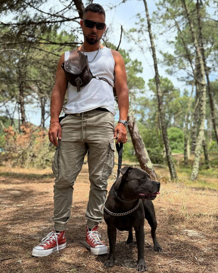 Man standing in forest holding leash of a dog known for a custom motorcycle capsule and love of the open road. Man standing in forest holding leash of a dog known for a custom motorcycle capsule and love of the open road.