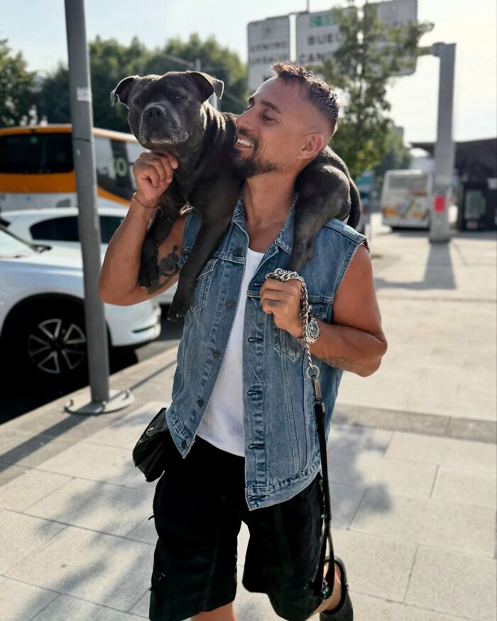 Man carrying dog on shoulders wearing denim vest outdoors, showcasing dog with custom motorcycle capsule love for open road. Man carrying dog on shoulders wearing denim vest outdoors, showcasing dog with custom motorcycle capsule love for open road.